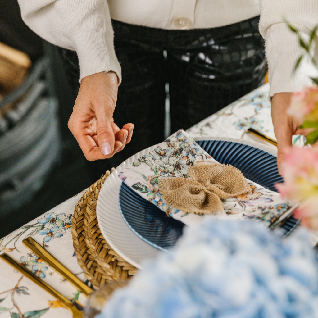 Hands placing a Wildflower Garden linen napkin on top of navy Denby starter plate.