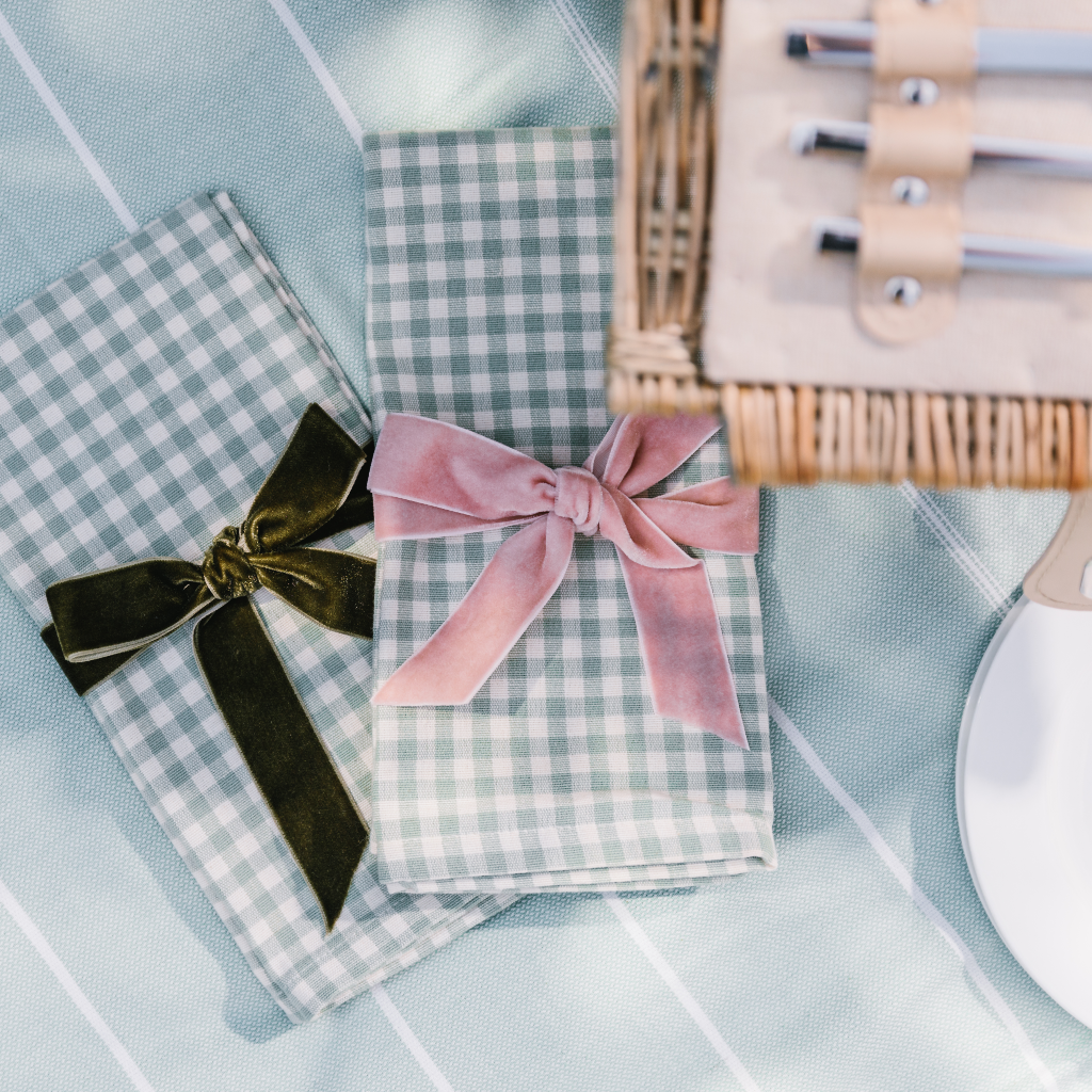 Mint green and cream gingham cotton napkins tied with a pink velvet and moss green velvet napkin bow. Set on mint green hamman throw