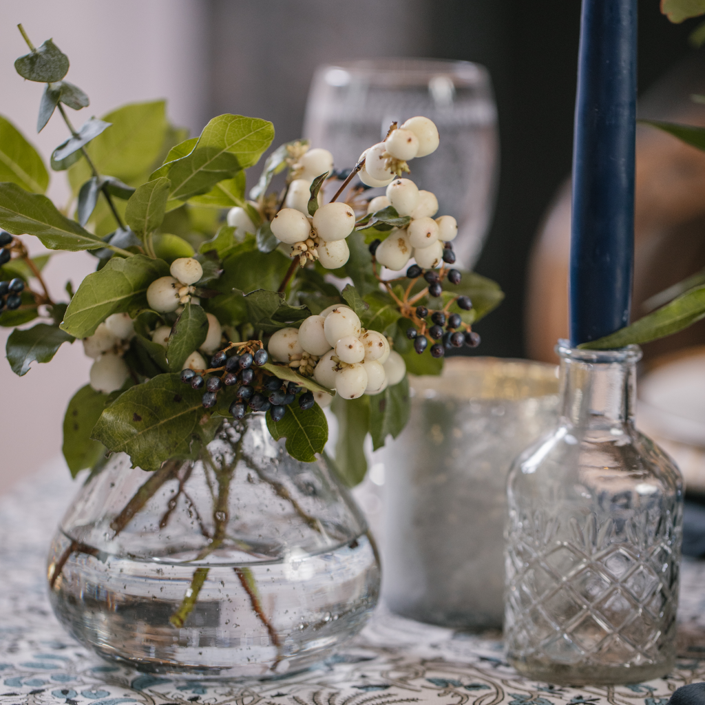 Detailed glass bud vase next to clear cut glass bottle candle holder and hand dipped navy tapered candle.