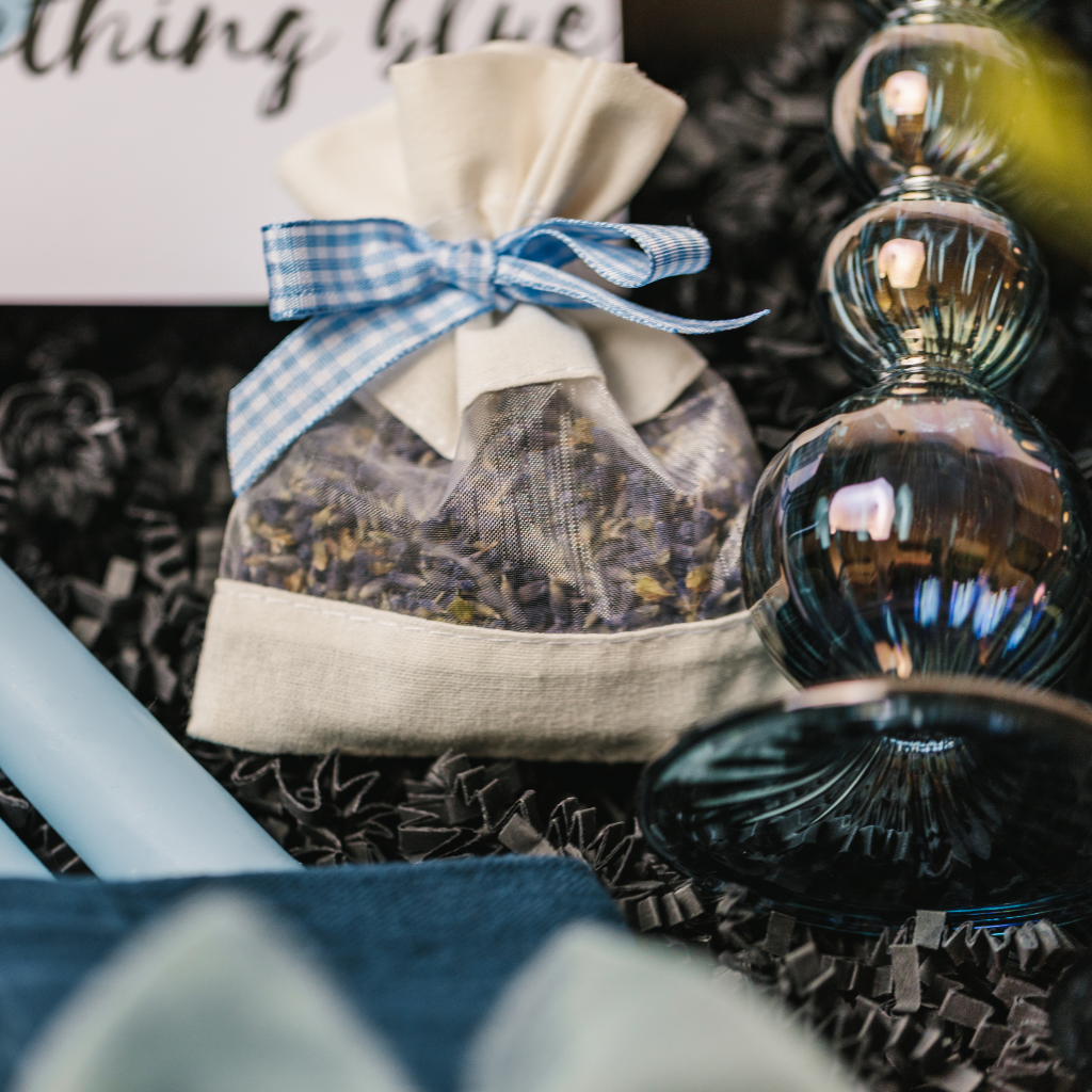 A pouch of dried lavender with blue gingham tie and the circular bottom of a blue glass candle holder