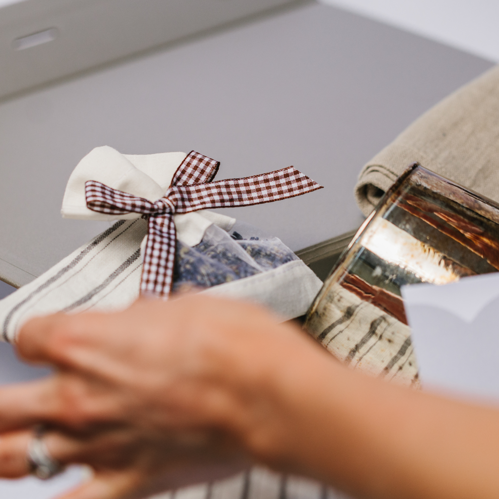 Hands organising a luxury gift box with close up of a lavender pouch tied with a gingham bow