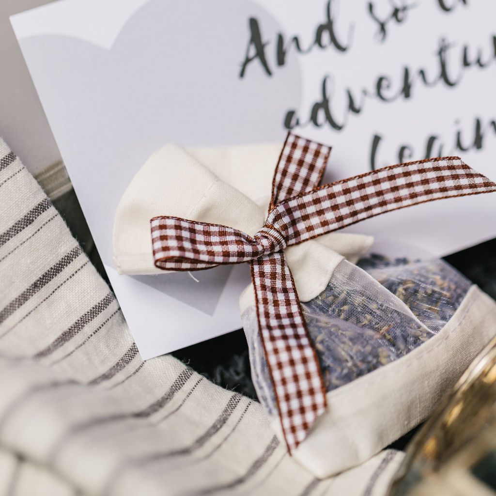 Image of lavender pouch tied with gingham ribbon including a wedding gift card and grey and white striped linen napkins