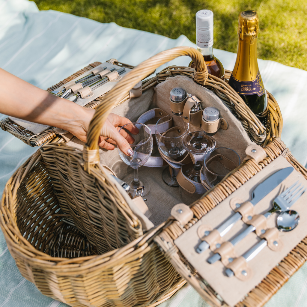 Reaching into fully fitted picnic hamper to get wine glasses which are next to fitted cutlery, salt and pepper pots and an ornate bottle stopper