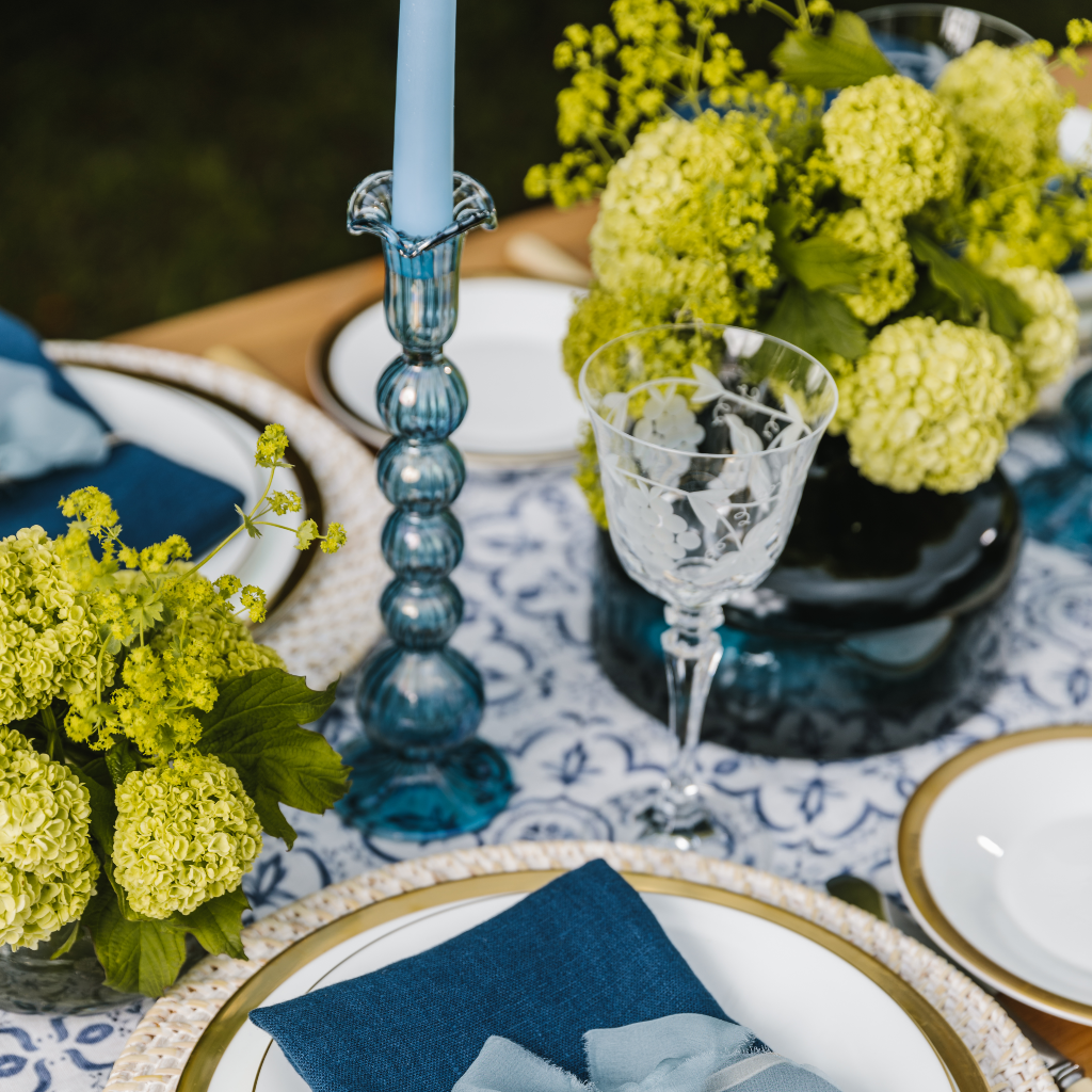 Blue glass candle holder with round orb detail and ruffled trim set next to large navy vase and mosaic detailed table runner.
