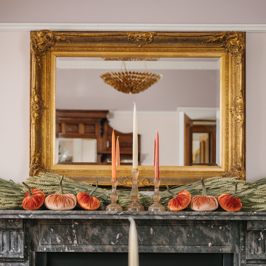 Autumn halloween mantlescape with trio of orange and ivory candles, velvet pumpkins and wheat bunches