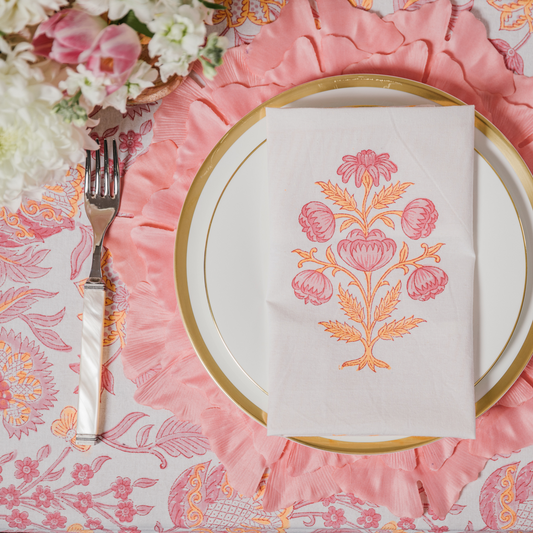 Coral floral leaf placemats layered with gold trimmed crockery, an Indian block print cotton napkin and pink patterned tablecloth