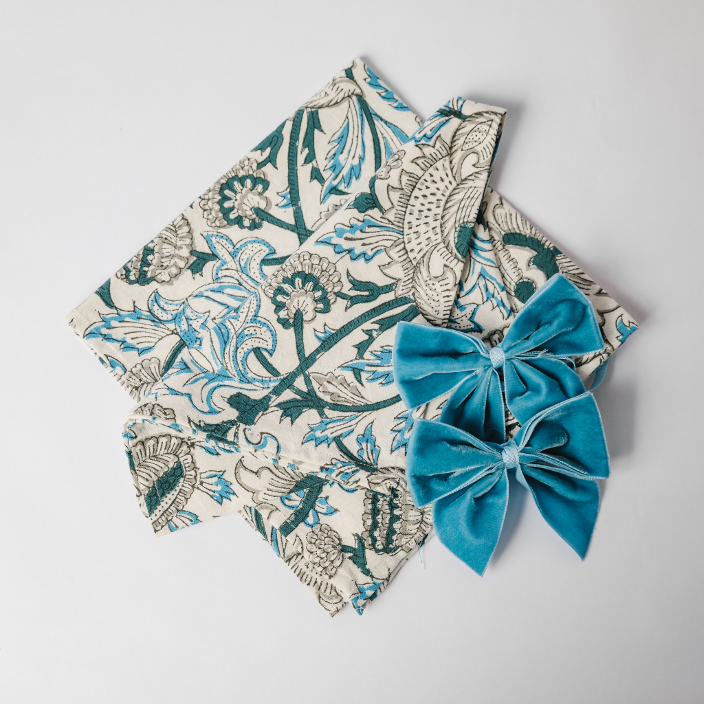 Navy blue, light blue and white block printed pattern cotton napkin folded next to kingfisher blue velvet napkin bows