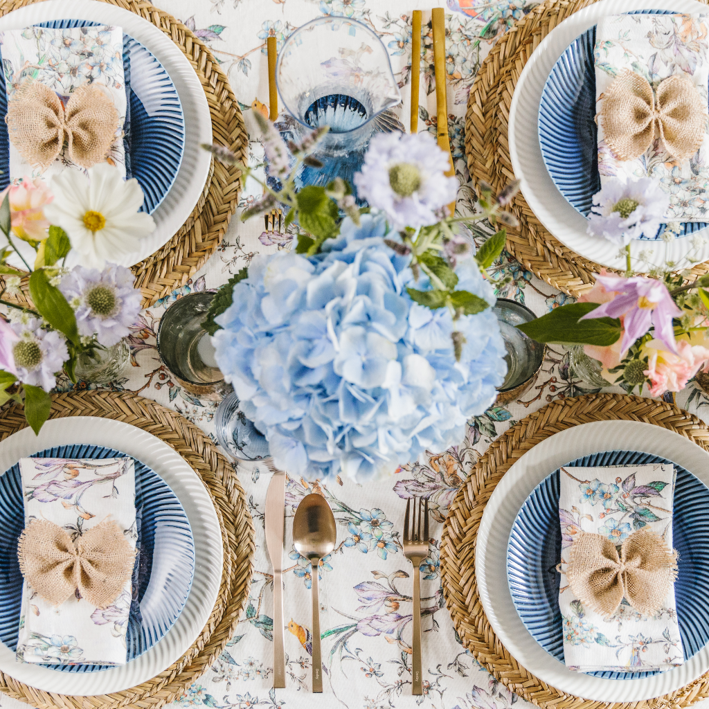 Top down view of four person Wildflower Tablescape - seagrass placemats, napkin bows, flora patterned table linen and copper candle holders.