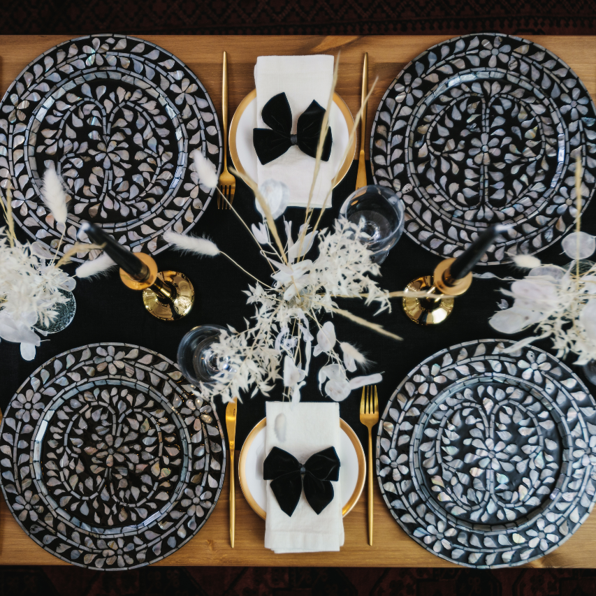 Birds eye view of Magical Monochrome tablescape-in-a-box collection with statement black and white mother of pearl inlay charger plates, white linen napkins with black velvet napkin bows, sleek brass candlesticks, black tapered dinner candles and dried flower and grass displays