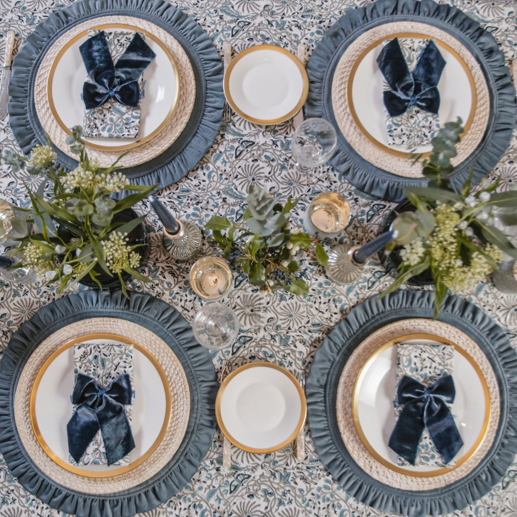Top down view of Twilight Tablescape four person setting with blue velvet ruffled placemats, Indian block printed table linens, navy blue velvet napkin bows and silver candlesticks.