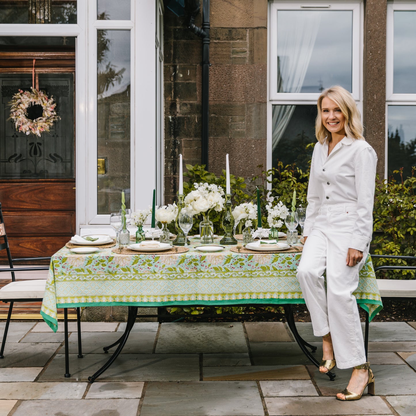 Kate Fairlie, founder of Truffle Tablescapes, next to the Mint & Moss tableware collection including green indian block print tablecloth, seagrass placemats, green glass candle holders, white linen napkins and green velvet napkin bows