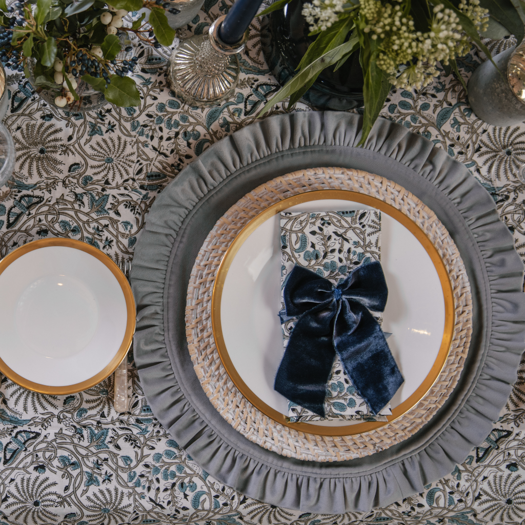 Birds eye view of place setting with luxury navy blue velvet napkin bows, Indian block printed table linen and a dove grey velvet ruffled placemat.