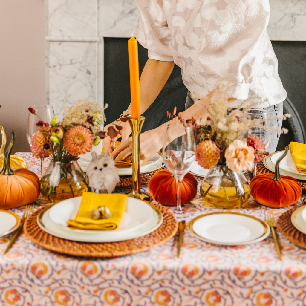 Setting a harvest tablecloth - hands placing feather owl next to velvet pumpkins, ochre linen napkins and brass candle holders