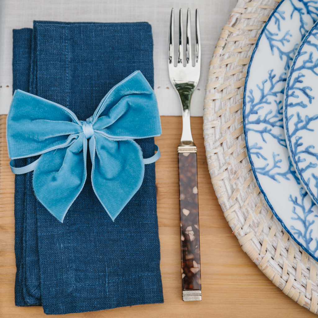 Tortoiseshell and silver fork next to navy linen folded napkin tied with kingfisher blue velvet napkin bow