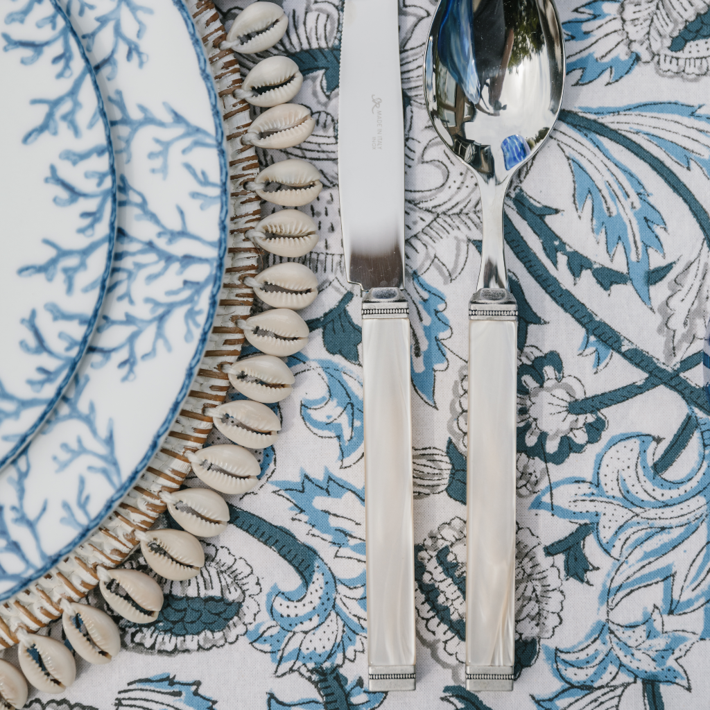 Blue and white coral design Santorini starter plate and main plate layered on a rattan and shell-trimmed placemat next to white pearl cutlery