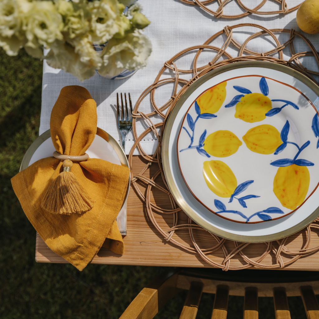 Top down image of lemon stoneware plate with blue twig design styled with mustard yellow napkin and ochre tassel napkin ring
