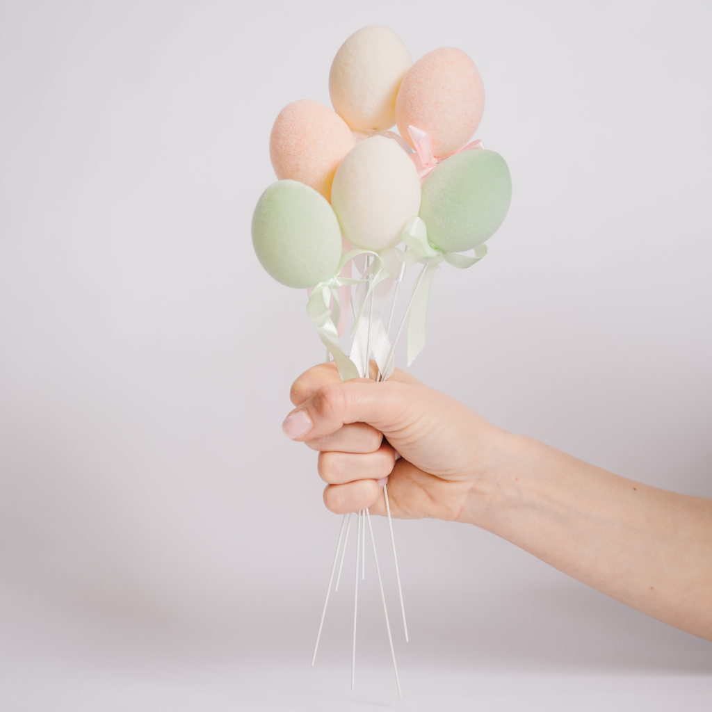 Hand holding a bouquet of flocked Easter egg decorations on wires with ribbon detail