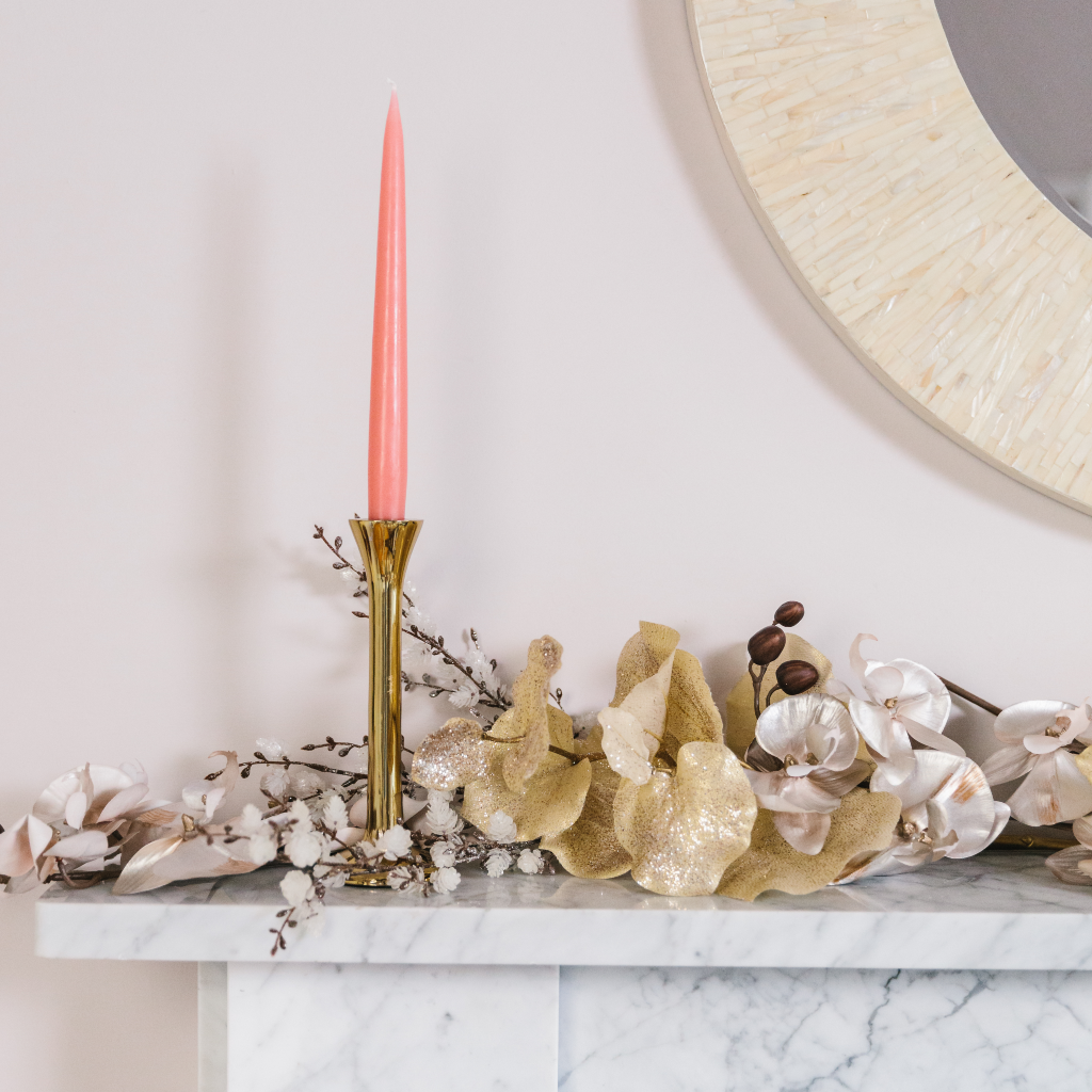 Vintage rose tapered dinner candle in sleek brass candlestick on top of a white marble mantle with gold garland display