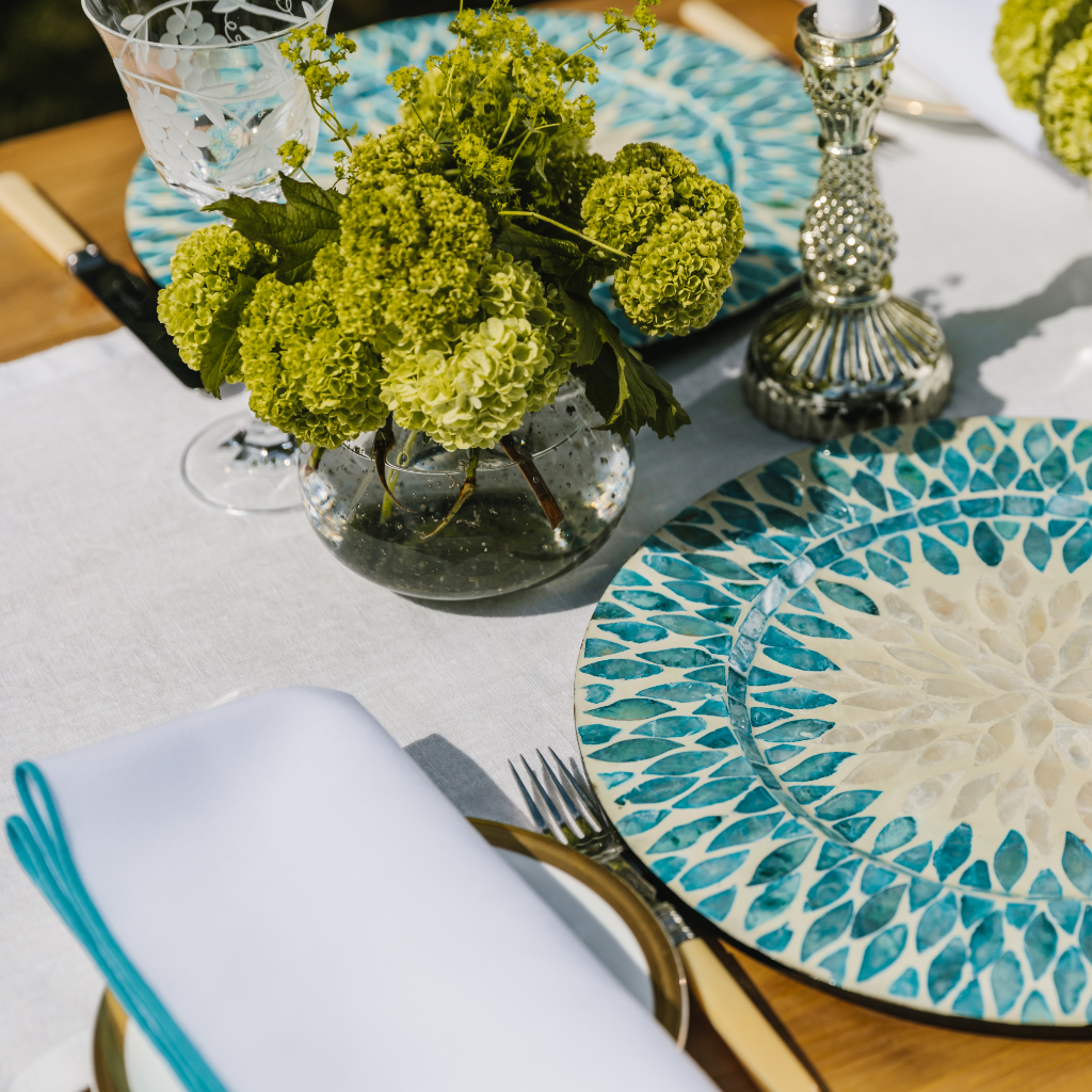 Crisp white linen table runner set in aqua mother of pearl charger plates, a clear glass bud vase and silver dinner candle holder