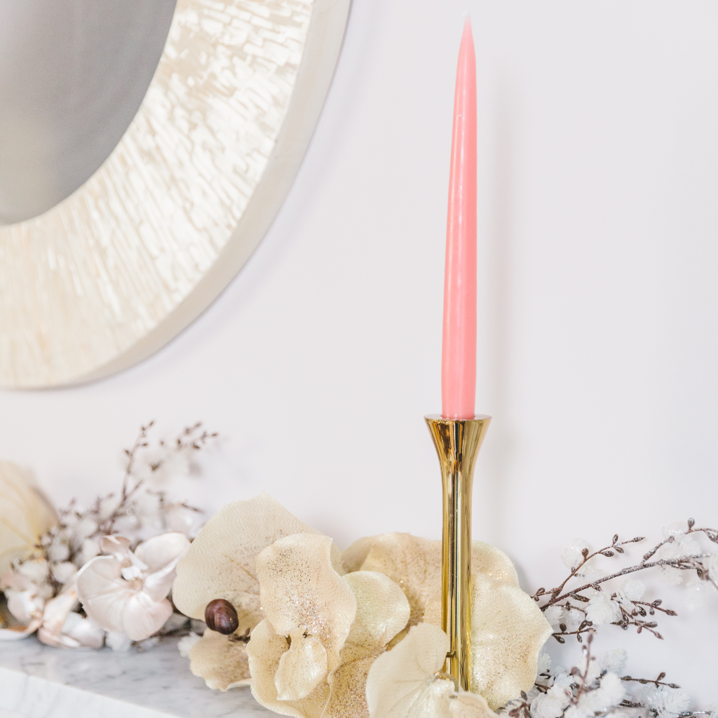 Vintage rose pink tapered dinner candle with gold brass candle holder next to garland and mother of pearl mirror edge