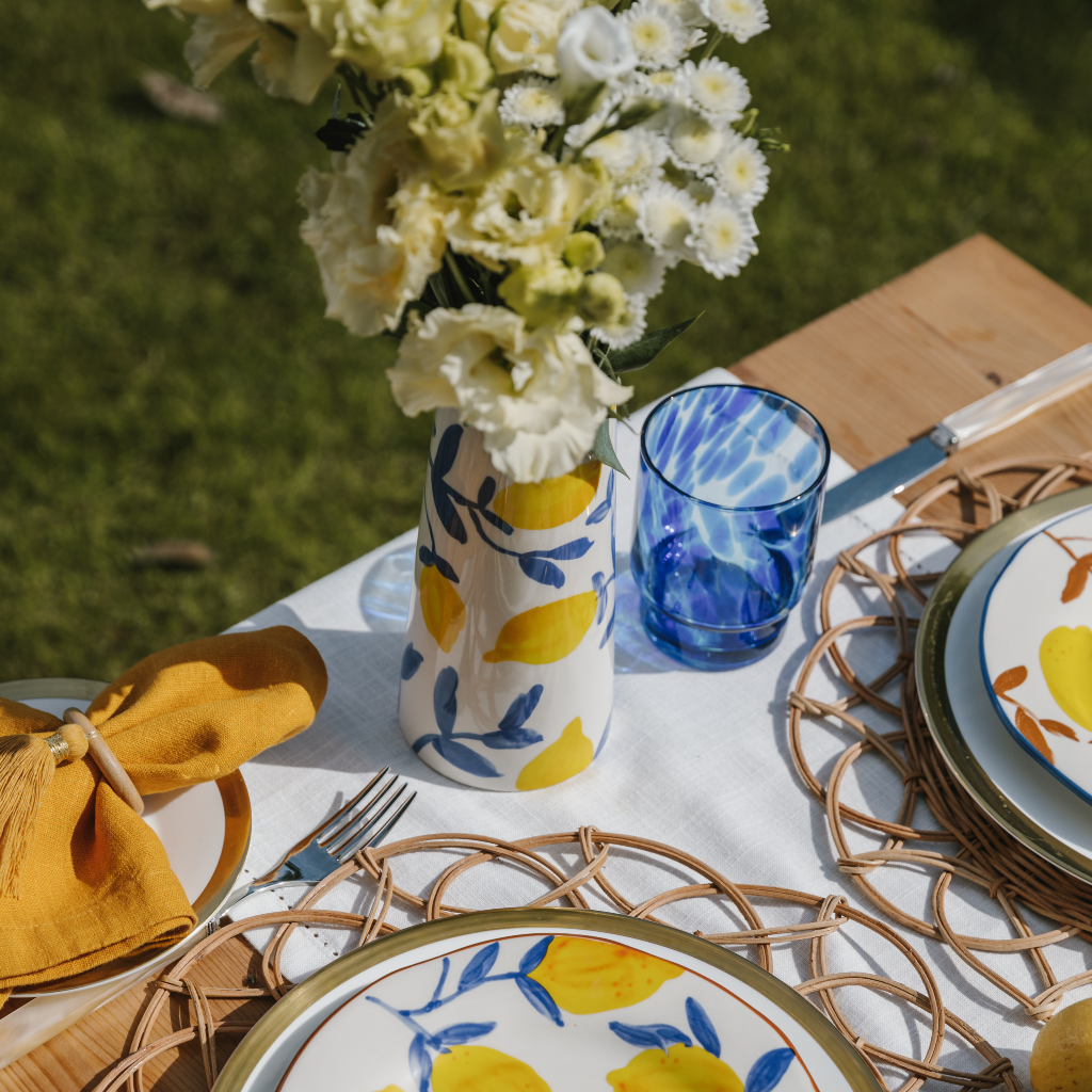 Lemon and blue design stone jug on Lemon Grove tablescape with white cotton runner and woven rattan placemats
