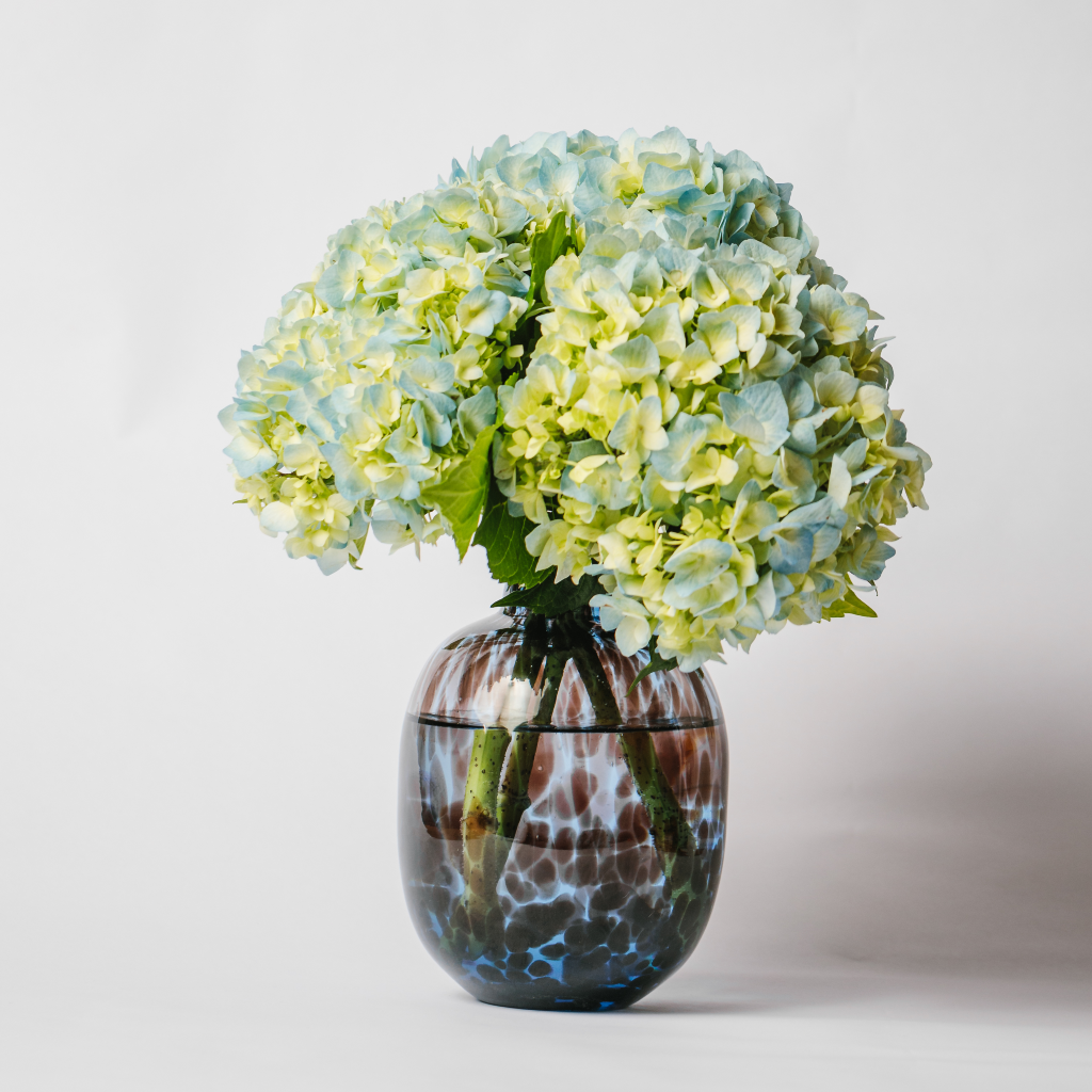 Large blue tortoiseshell leopard glass vase with posy of blue and green hydrangea