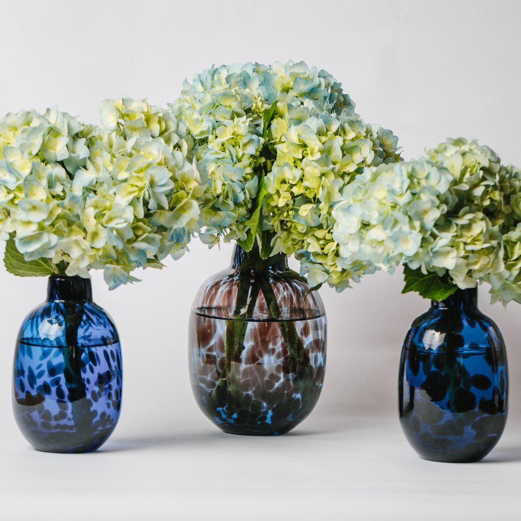 Trio of blue dappled leopard glass vases with blue and green hydrangea