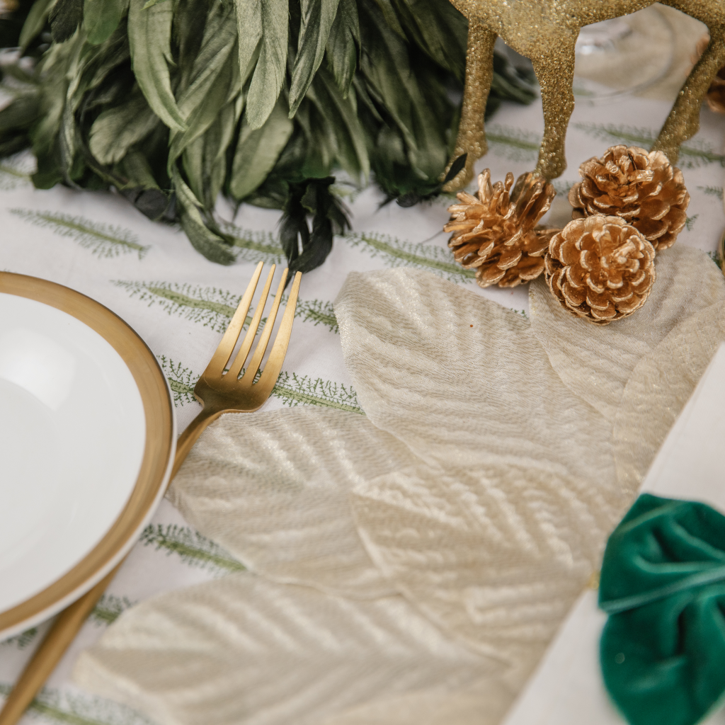 Forest green Christmas place setting with champagne gold placemat, gold fork and golden pine cones