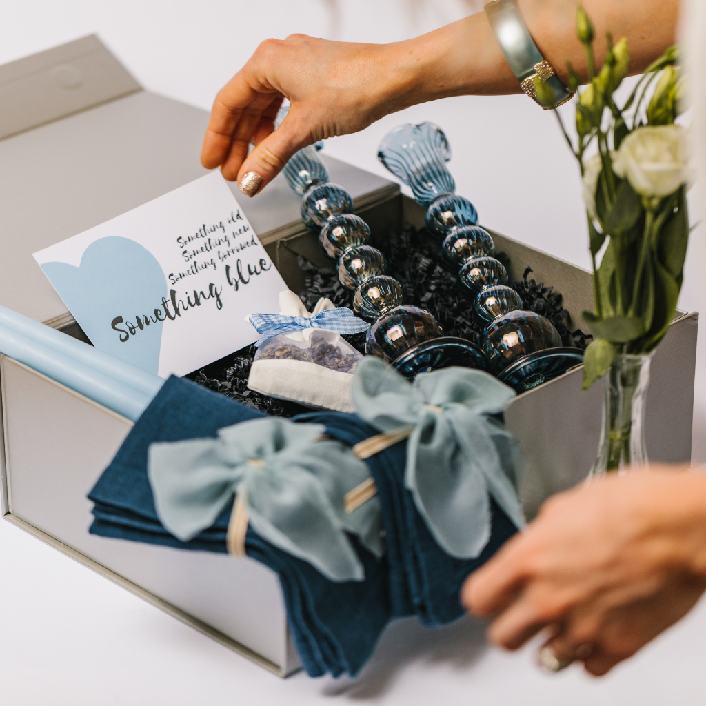 Hands sorting a luxury silver wedding gift box with blue tableware display including linen napkins, napkin bows and Egyptian hand blown candle holders