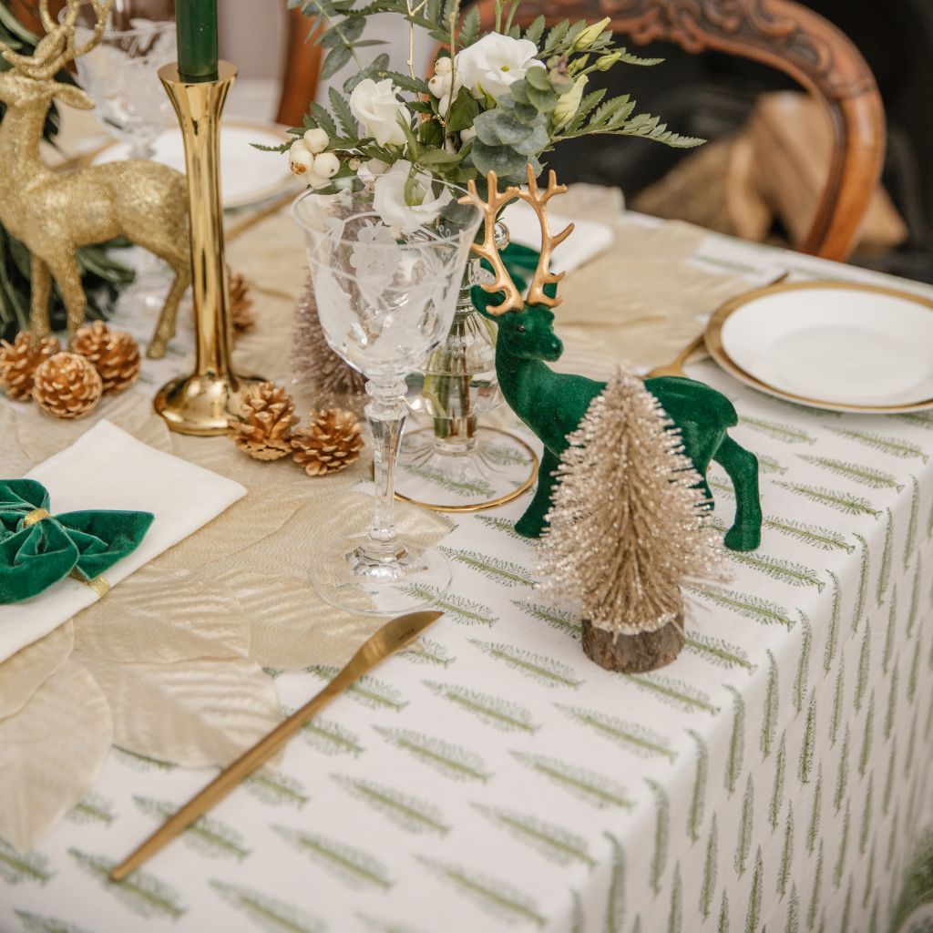 Green tablescape featuring forest green flocked stag, gold brush trees, champgane gold leap placemats, Indian block printed tablecloth and gold pine cones
