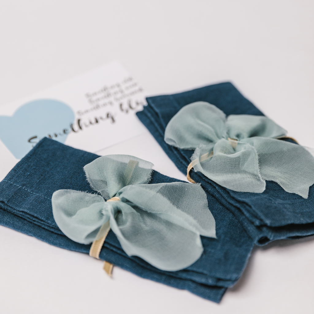 100% linen napkins in navy tied with raw edge silk napkin bows and a personalised wedding gift card in the background
