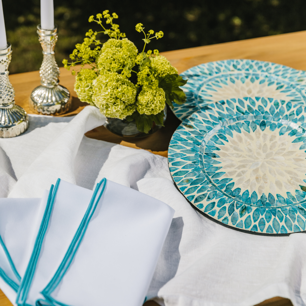 Aqua Pearl tableware collection set out with white linen table runner, aqua embroidered napkins, mother of pearl charger plates and ornate silver candle holders