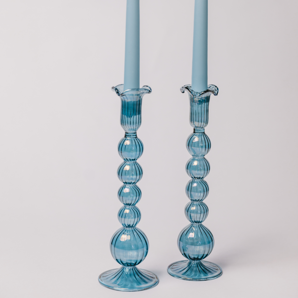 A duo of hand blown powder blue glass candlesticks displayed with pastel blue tapered dinner candles