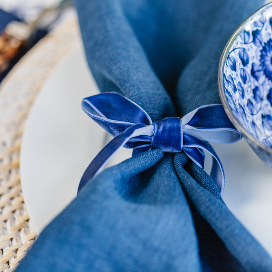 Close-up image of 100% linen navy dinner napkin tied with a blue velvet ribbon bow.