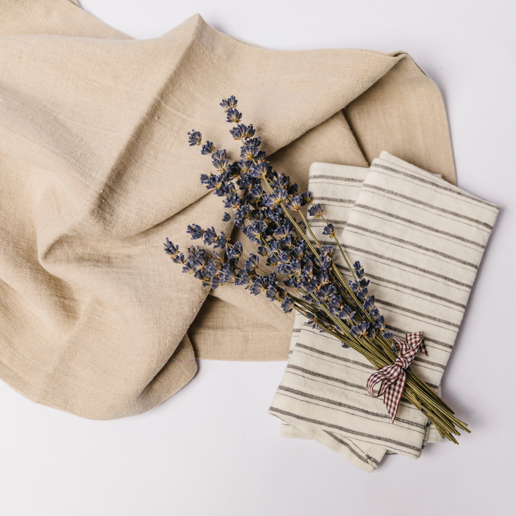 A natural coloured 100% linen table runner with grey and white striped linen napkins and a posy of dried lavender tied with a brown gingham bow