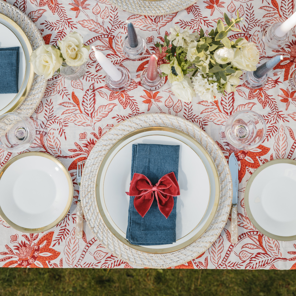 Red, white and blue place setting with white rattan charger plate, blue linen napkins and deep red velvet napkin bows