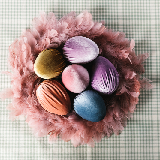Dusky pink feather Easter wreath filled with large pastel coloured velvet eggs and placed on top of a duck egg gingham tablecloth