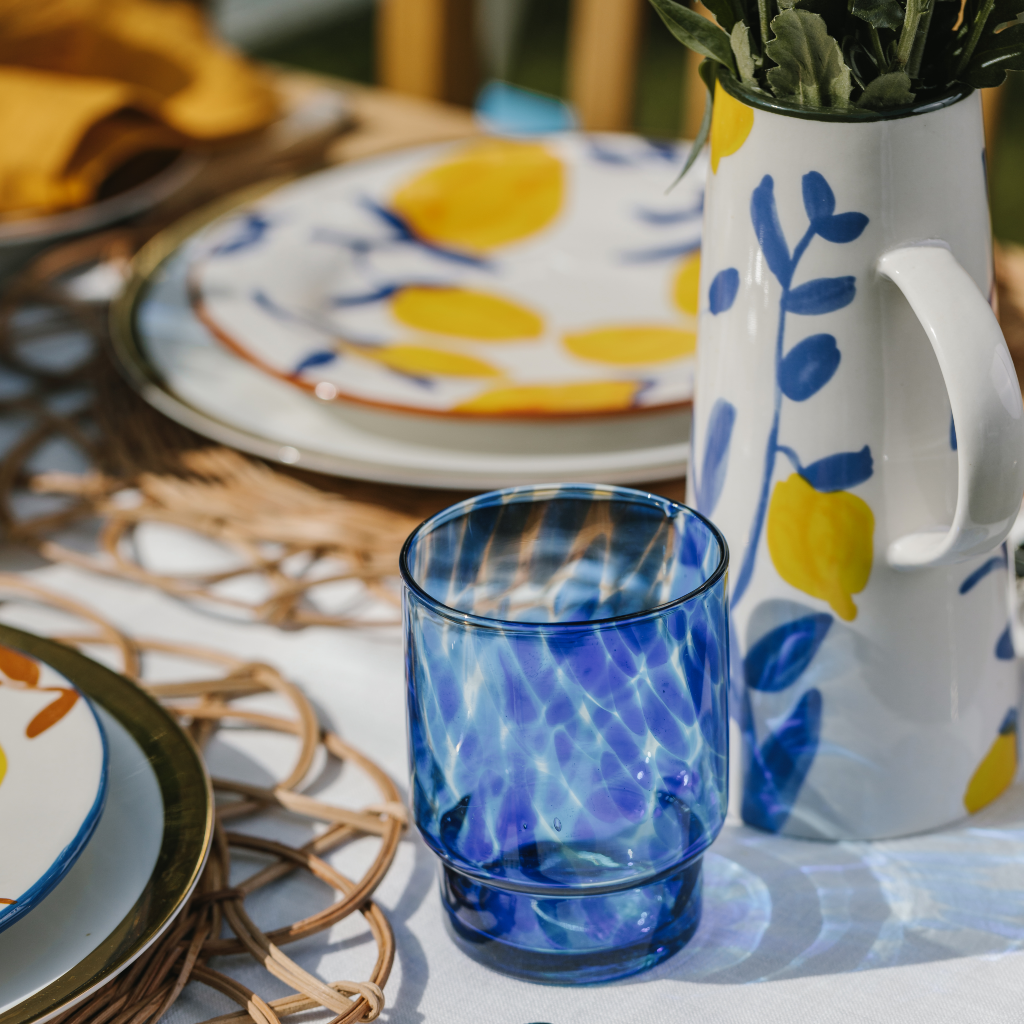 Yellow lemon stoneware carafe jug with blue painted vine detail sitting next to blue dappled tumbler glass