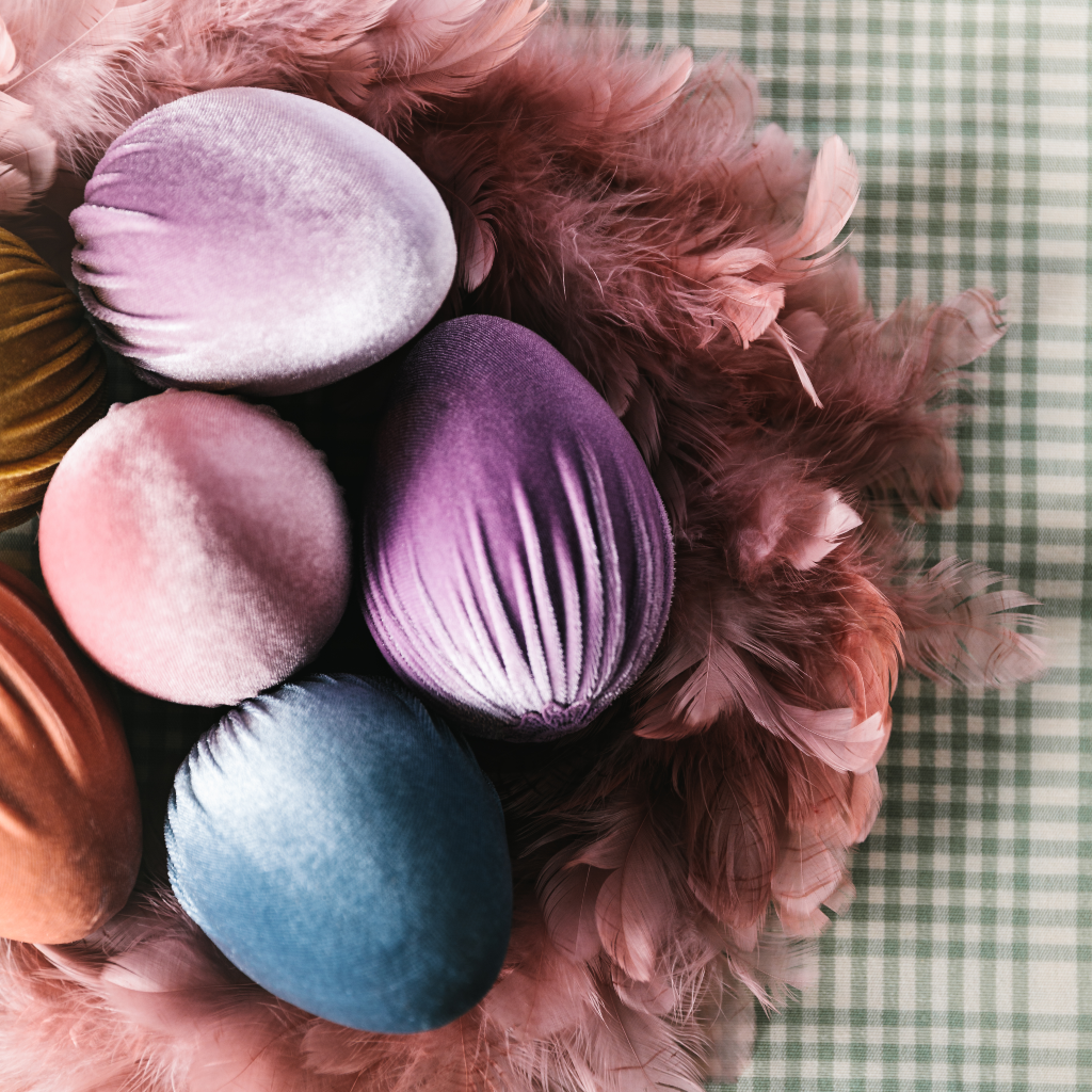 Blue, lilac, peach, pink and soft gold velvet ostrich egg decorations displayed within a ducky pink feather wreath on top of a duck egg and cream gingham tablecloth