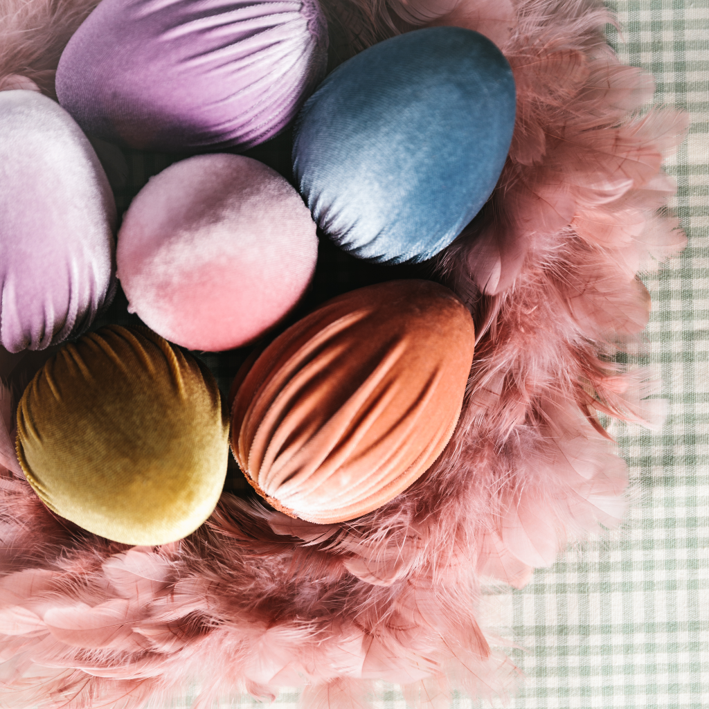 Blue, lilac, peach, pink and soft gold velvet ostrich egg decorations displayed within a ducky pink feather wreath on top of a duck egg and cream gingham tablecloth