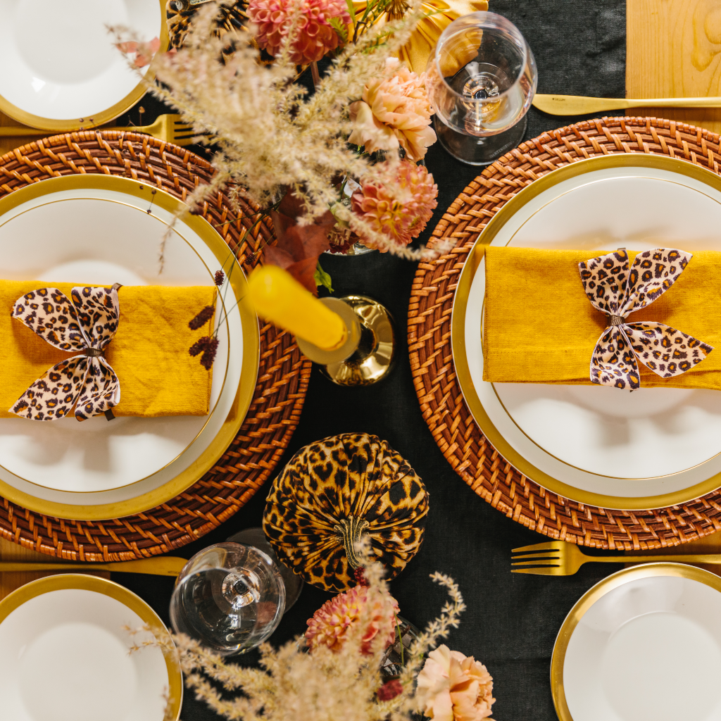 Top down view of Hallowe'en tablescape with ochre linen napkins, black table runner and leopard print napkin bows and pumpkins