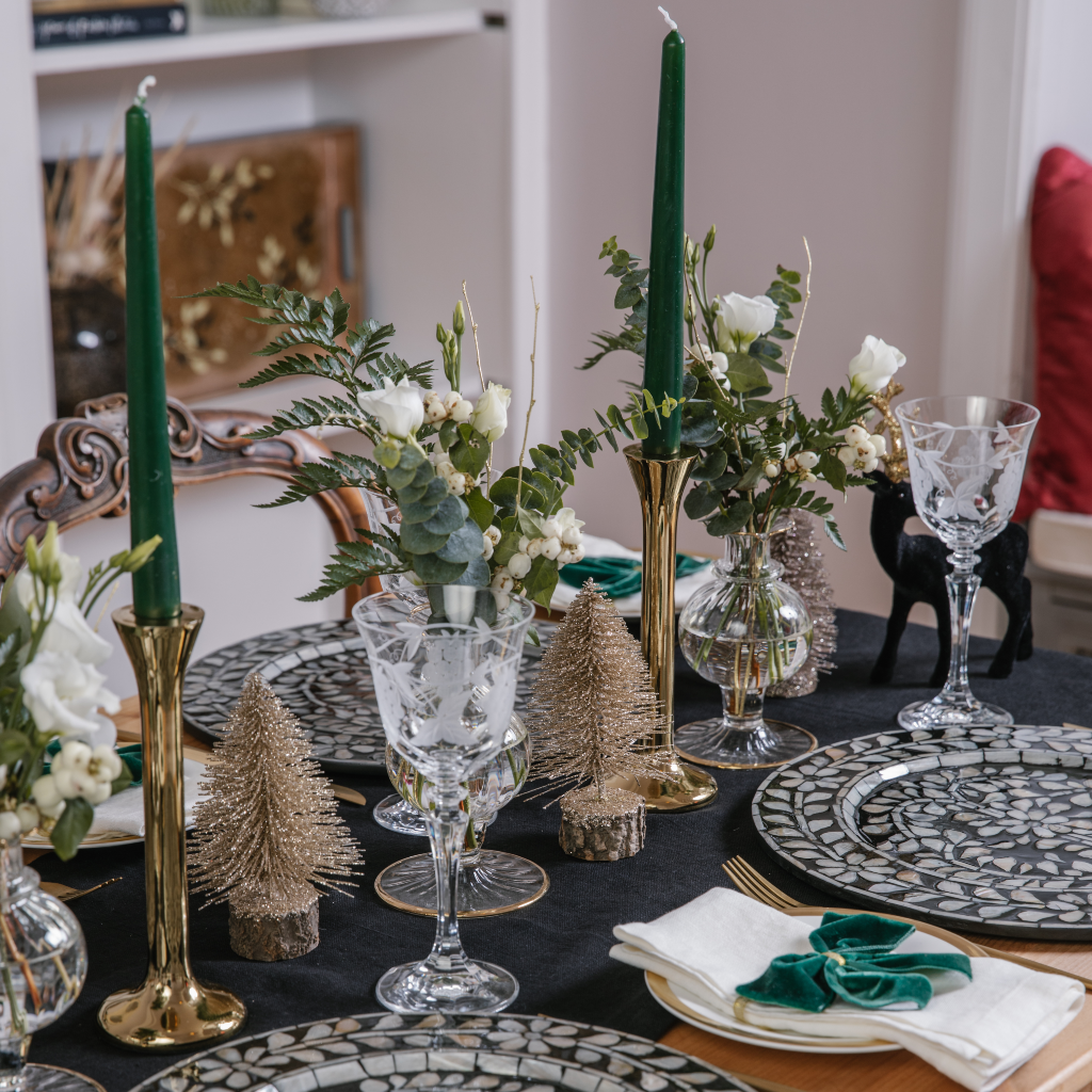 Monochrome tablescape with brass candlesticks, forest green tapered candles, gold glitter brush trees, bud vases and flocked black stag decorations