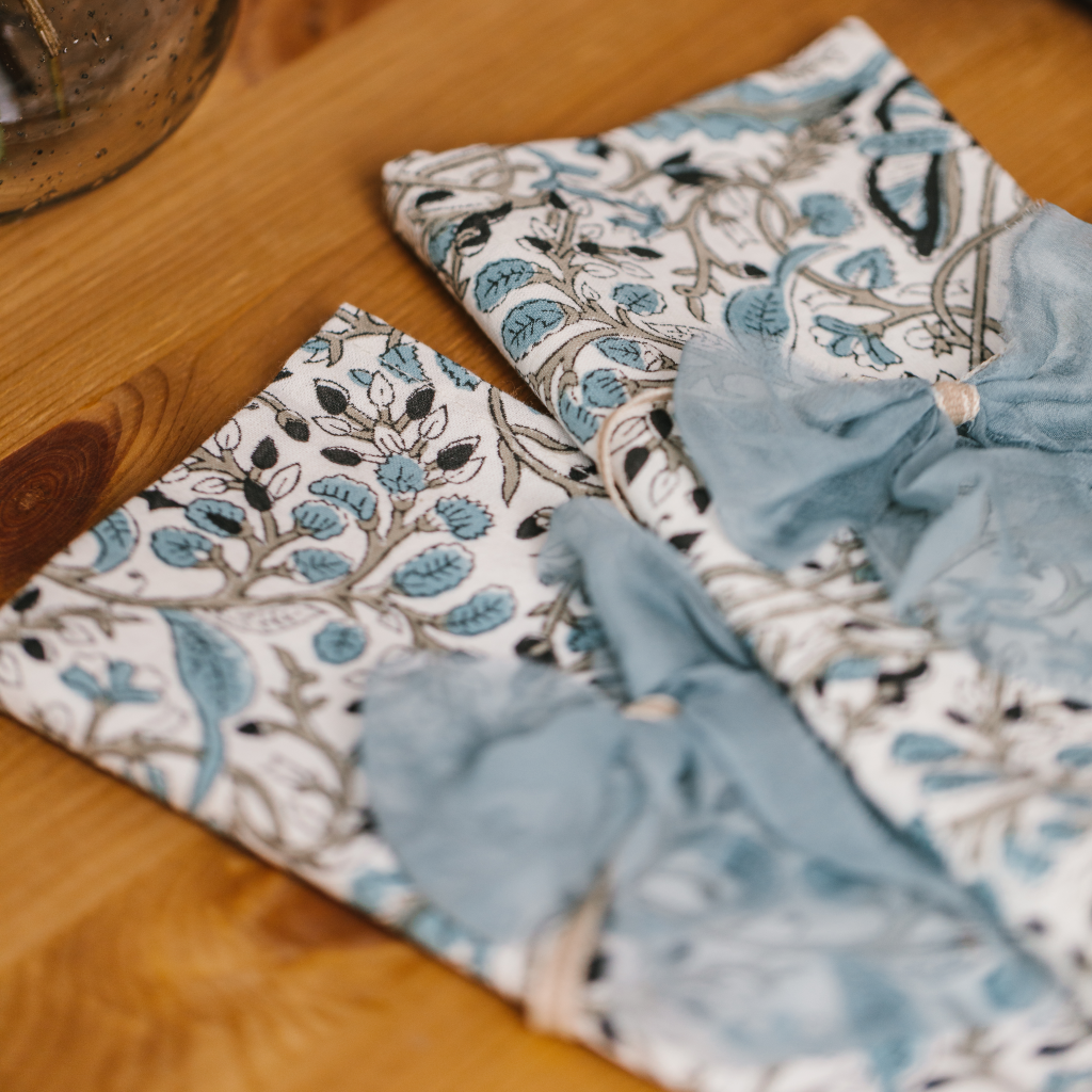 Close-up view of navy, blue and white Indian block printed folded napkins and pale blue raw edge silk napkin bows.