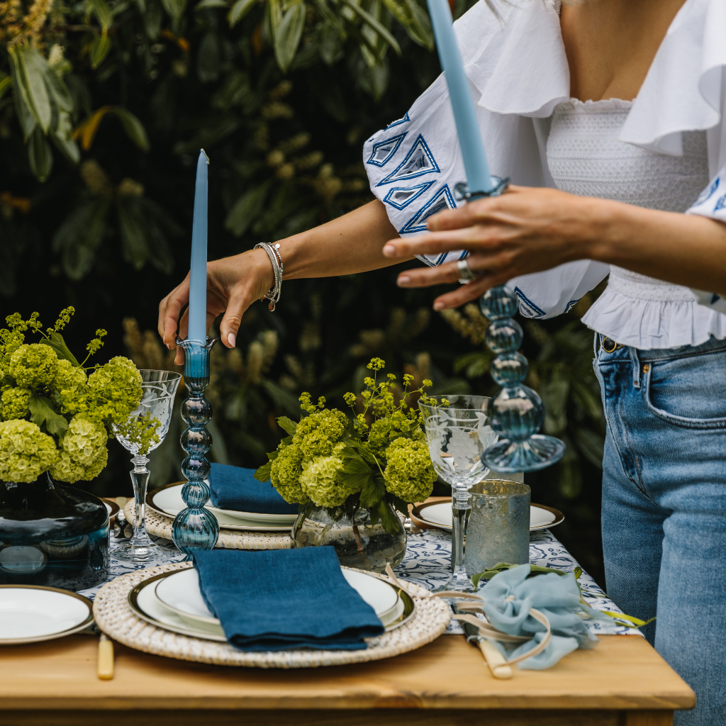Kate Fairlie, director of Truffle Tablescapes, placing two powder blue glass candle holders with pale blue tapered candles onto summer mosaic tablescape.