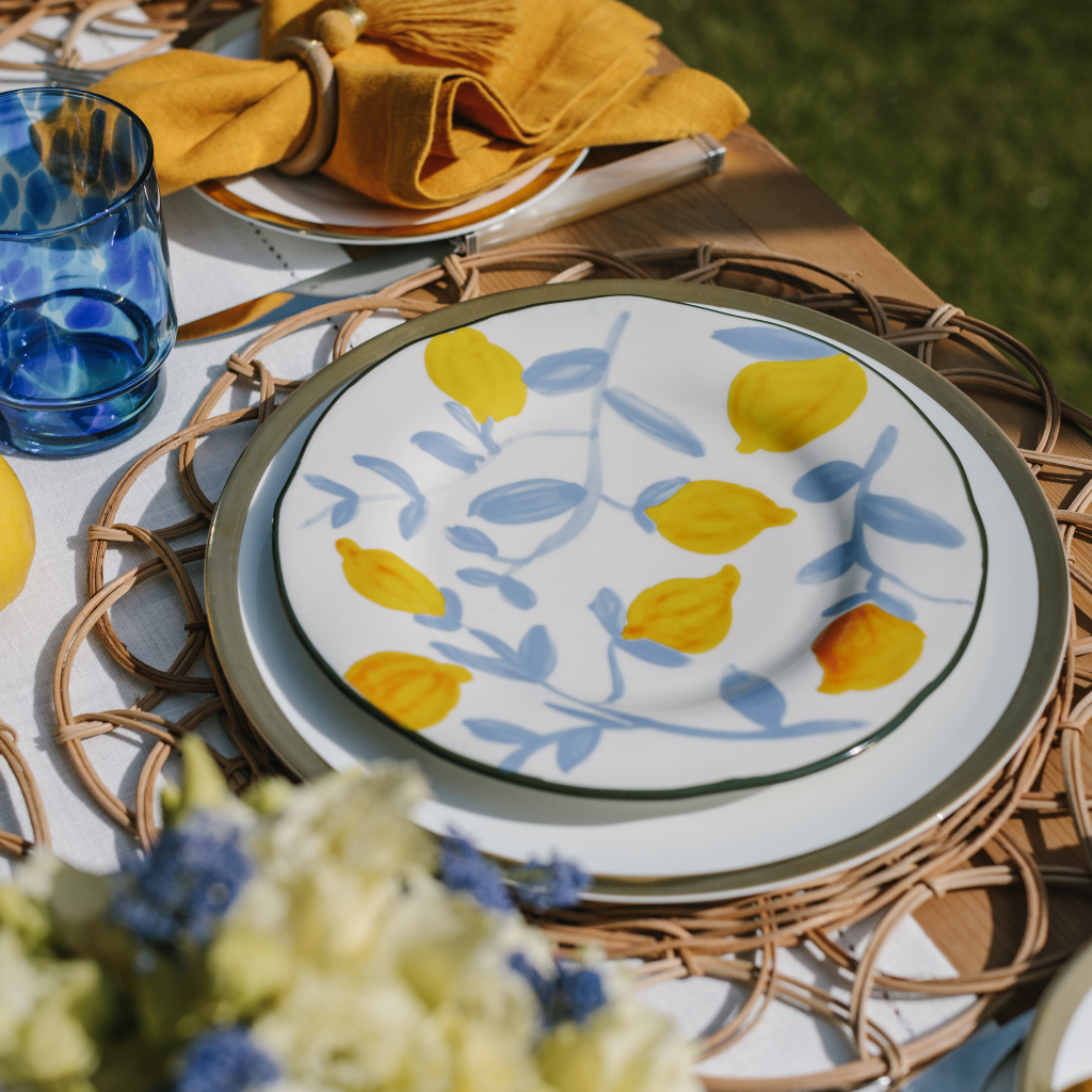 Yellow lemon plate with blue twig design set on a gold trim main plate and brown woven rattan placemat