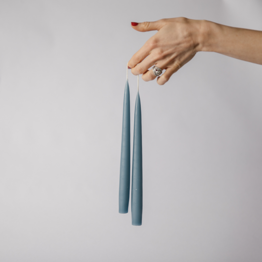 Hand holding a set of two grey blue tapered dinner candles in the air