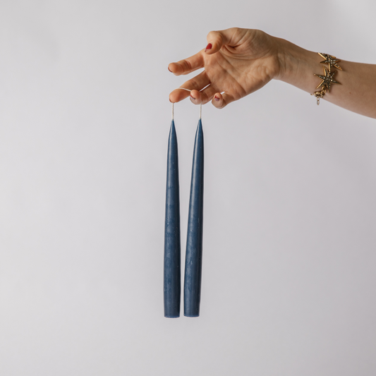 Hand holding two navy hand dipped tapered dinner candles