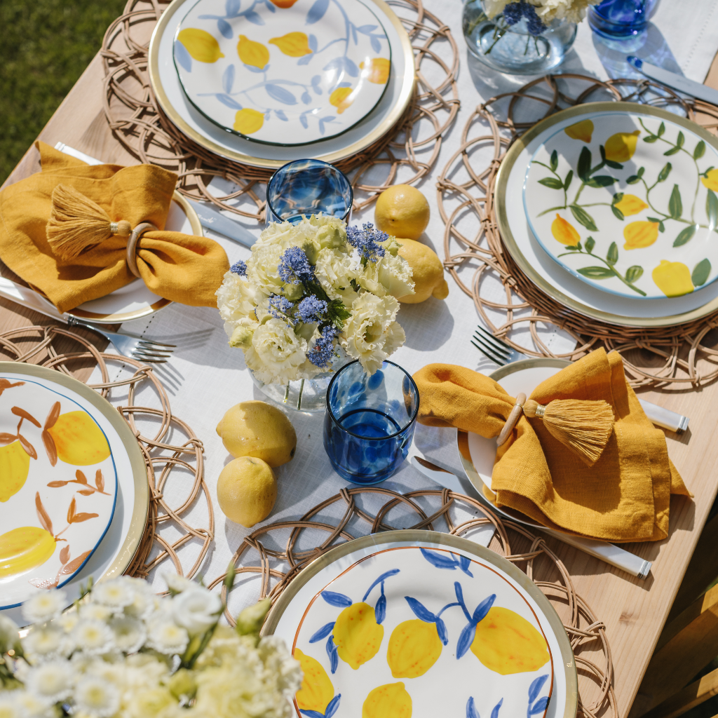 The Lemon Grove tablescape featuring four mismatched lemon design plates, mustard yellow napkins, ochre tassel napkin rings and blue dappled glassware