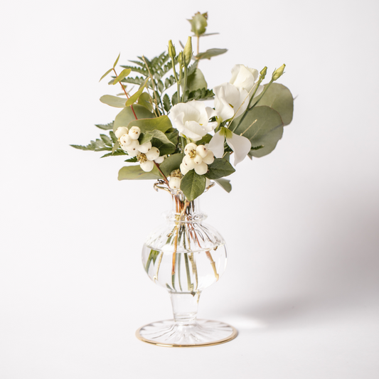 Hand blown clear glass bud vase with gold ruffled trims. The vase is set on a white background and is displaying white flowers with evergreen foliage.