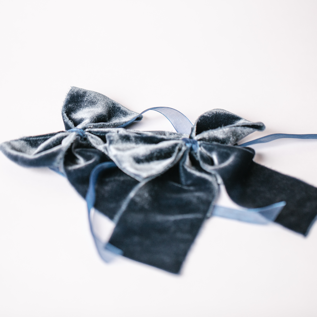 Navy blue velvet napkin bows with ribbon ties laid out on white background.
